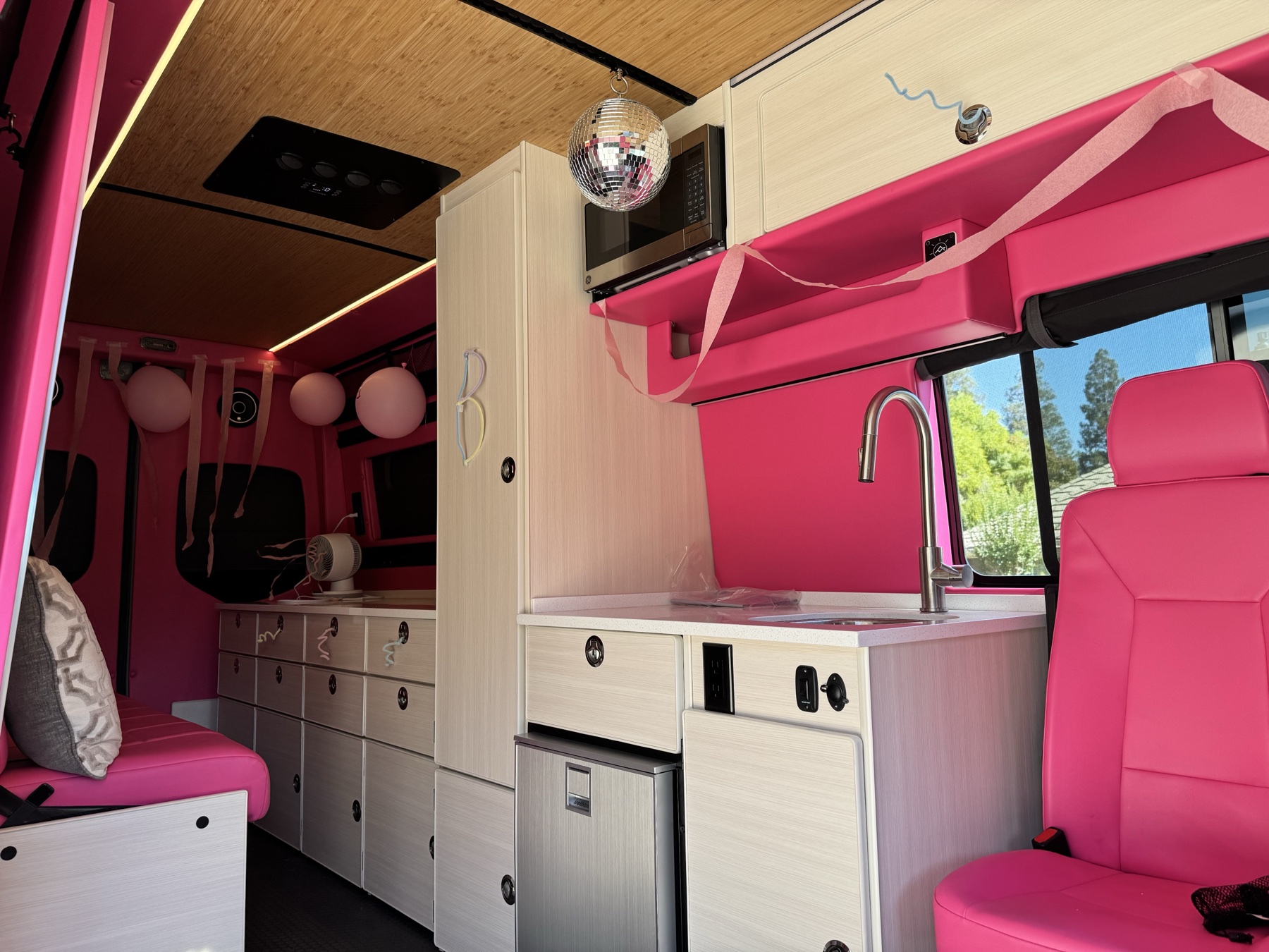 Luxury pink Dream Van party interior with disco ball, microwave, sink, and seating in California